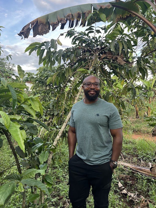 Ben Serunyigo, founder of Nyaliko, standing among coffee trees on a Ugandan farm
